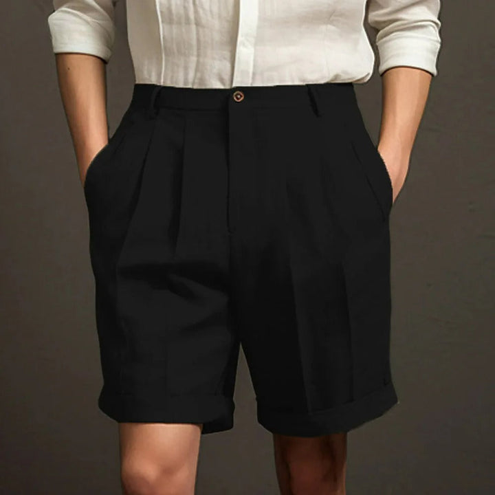 Person wearing a white button-up shirt with sleeves rolled up and high-waisted breathable linen shorts, standing with hands in pockets against a plain dark background—a perfect look for summer.