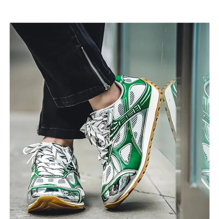 A person wearing black pants and sporty sneakers with green, white, and silver details stands near a glass surface. The lightweight mesh shoes feature patterned laces, a cushioned insole, and tan-colored rubber soles.