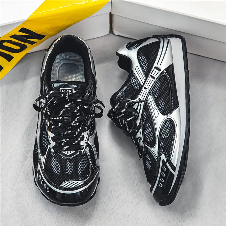 A pair of black and silver athletic sneakers with cushioned insoles and mesh panels are displayed on a light surface, near a white box and yellow caution tape. Patterned laces add style to these lightweight mesh shoes.