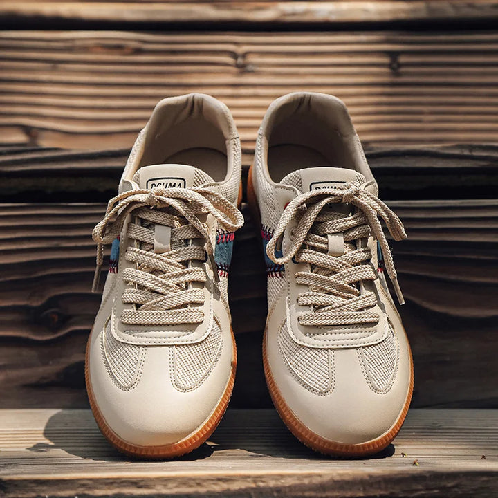 A pair of lightweight breathable sneakers with tan laces and gum soles sits on wooden steps, viewed from above. The shoes feature mesh details, a colorful plaid accent near the laces, and EVA midsole cushioning for added comfort.