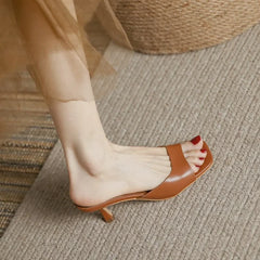 A person wearing a brown genuine leather open-toe heeled sandal with red nail polish on their toenails, standing on a textured beige carpet.