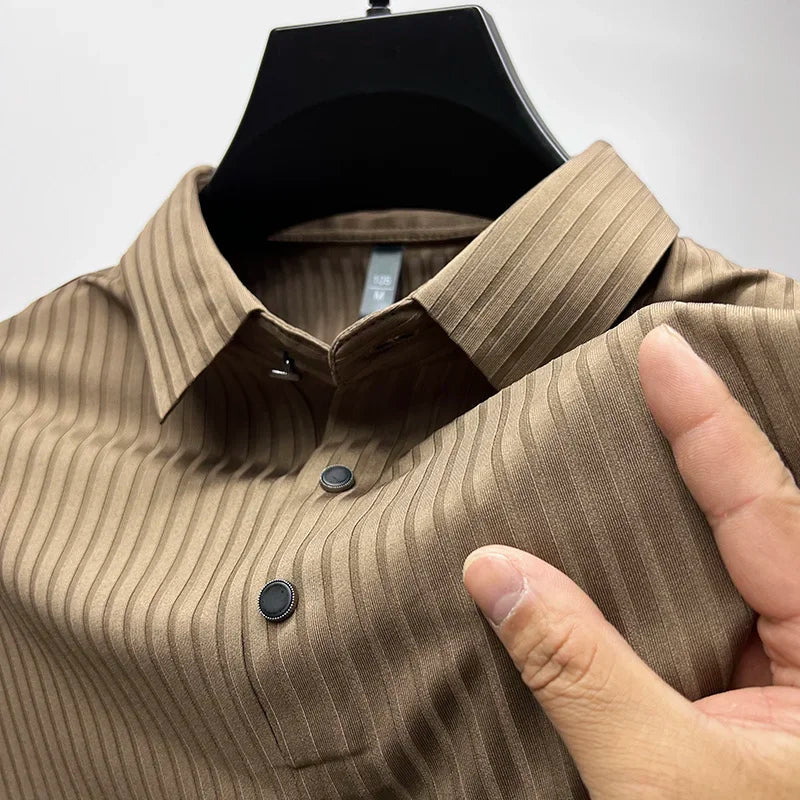A hand holds the sleeve of a brown, pinstriped, long-sleeve shirt on a hanger, highlighting its natural temperature regulation and button details near the chest.