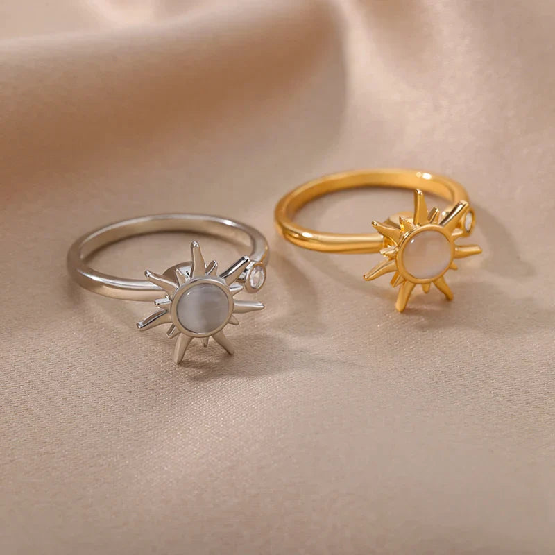 Two rings on beige satin: one silver sun ring with a white center and small clear stone, and one adjustable gold ring featuring a sun-shaped design. These elegant pieces evoke warmth and radiance for any look.