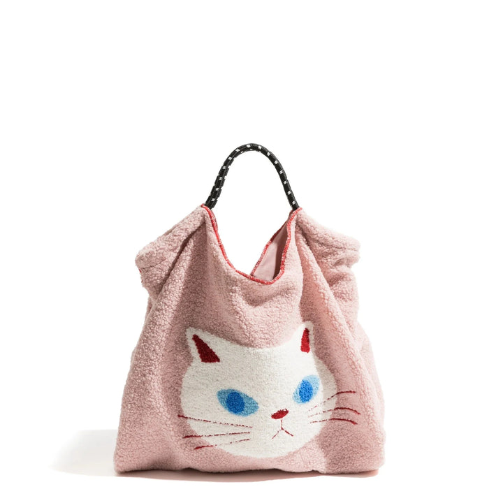 A pink faux fur handbag with a black handle, featuring a large white cat face with blue eyes, pink ears, and a red nose and mouth on the front—perfect for fans of animal pattern totes.