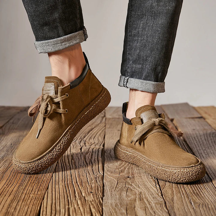 A person wearing rolled-up dark jeans and tan men's Chaussure Homme shoes in supple cow suede leather with thick textured soles, standing on a wooden floor.