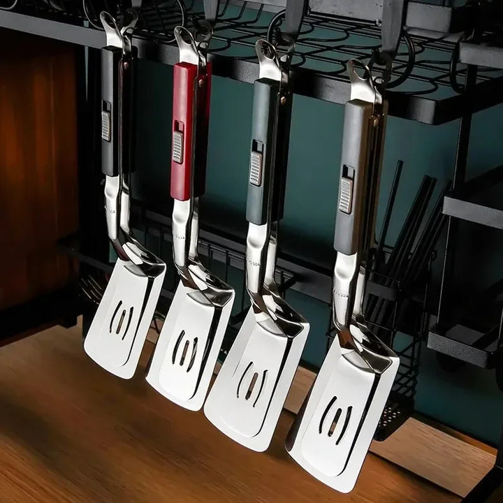 Four metal grilling tools with colored handles (black, red, green, and gray) hang on a black rack above a wooden countertop—perfect additions for BBQ season in any kitchen setting.