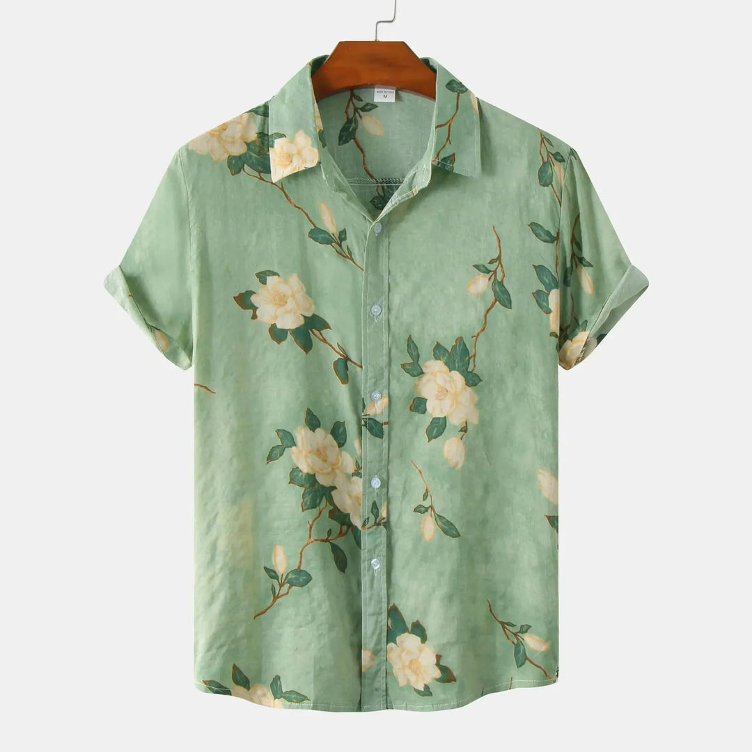 A light green floral shirt with white and yellow flowers and green leaves, perfect for summer style. This linen shirt features short sleeves, button-up front, and is displayed on a wooden hanger against a white background.