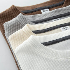 Four heavyweight long-sleeve shirts in brown, gray, beige, and white are neatly stacked in a diagonal arrangement, highlighting their waffle knit texture and Uniqlo labels for a premium cotton feel.