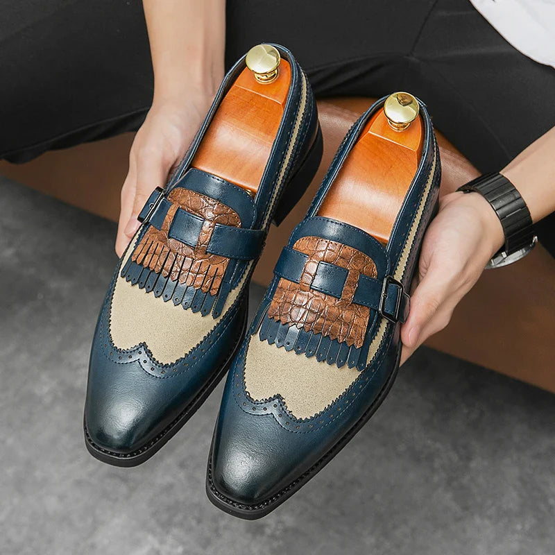 A person holds a pair of stylish mens loafers featuring premium leather shoes in blue, tan fabric, and brown textured accents with fringe detailing and strap accents, viewed from above.
