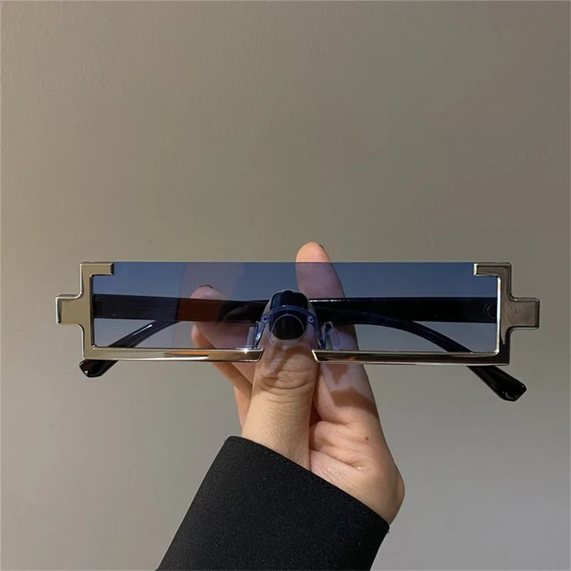 A hand holds a pair of rectangular, blue-tinted sunglasses with a geometric, angular frame design against a plain, light-colored background. These lightweight shades offer UV400 protection for your eyes.