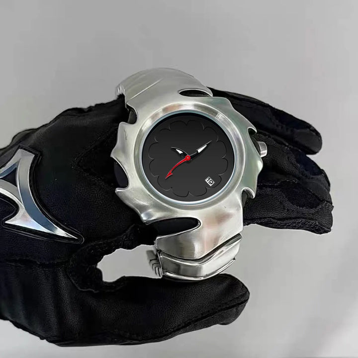 A person wearing a black glove with a silver pattern is holding a stainless steel, water-resistant wristwatch featuring a jagged, flame-like bezel, black dial, red hands, and a small date display.