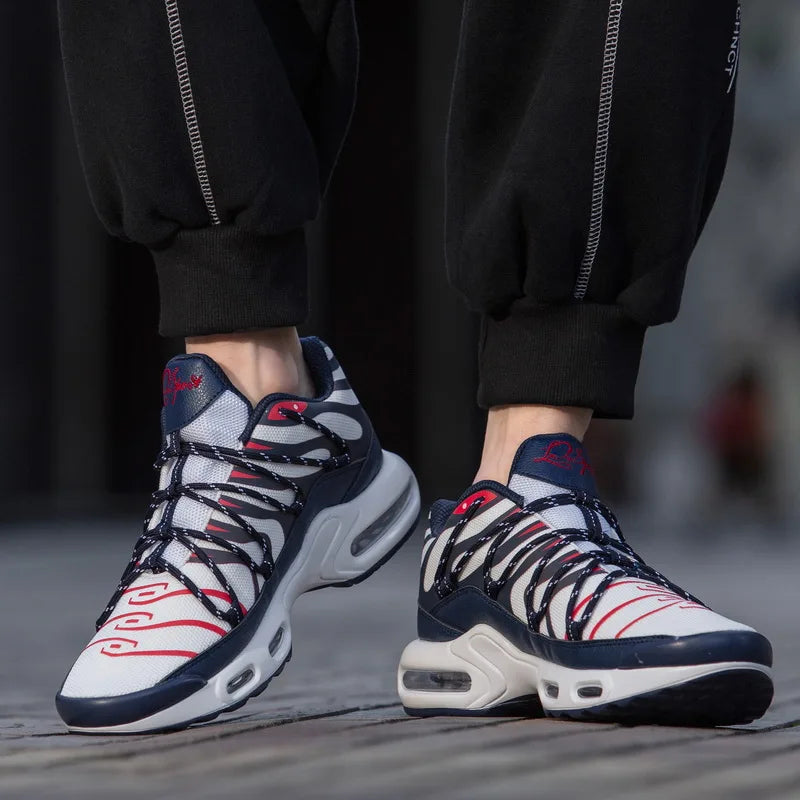 A person wearing black joggers and stylish athletic sneakers with a white, navy blue, and red design stands on a wooden surface. The shoes feature unique side lacing, a cushioned midsole, and a chunky, durable traction outsole.