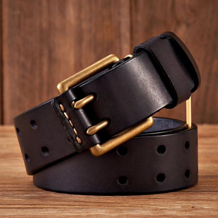 A coiled black cowhide leather belt with a brass-colored rectangular buckle, featuring multiple holes along its length, is displayed on a wooden surface with a wooden background.