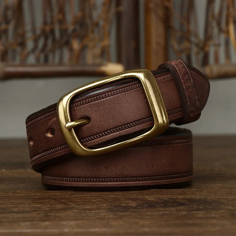 A coiled cowhide belt with a rectangular brass buckle is displayed on a wooden surface, with a woven background partially visible behind it.