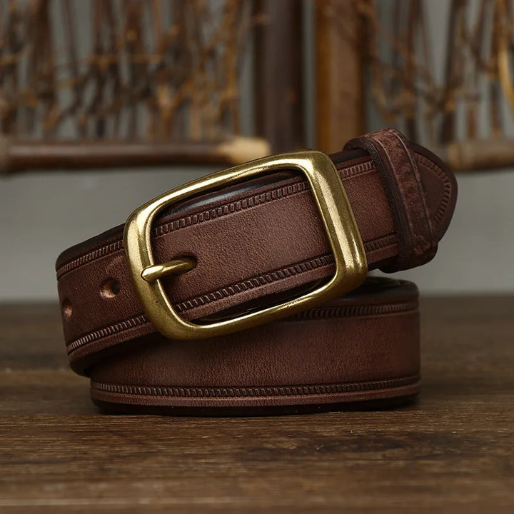 A coiled cowhide belt with a rectangular brass buckle is displayed on a wooden surface, with a woven background partially visible behind it.