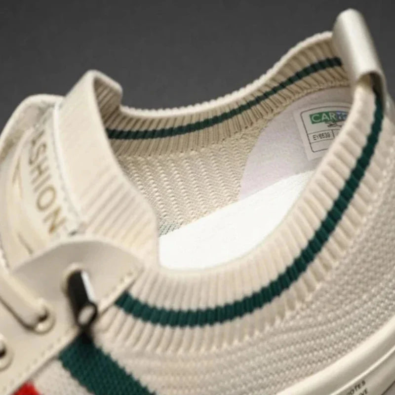 Close-up of a beige knit sneaker with green and red stripes, cream laces, and a white label inside the heel area. Features a durable rubber outsole for long-lasting wear. The word FASHION is partially visible on the tongue.