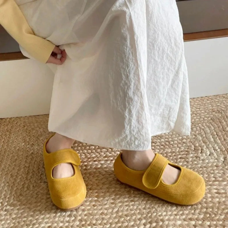A person wearing a long white skirt and yellow Mary Janes stands on a woven beige rug, showcasing stylish women casual shoes perfect for any relaxed occasion.