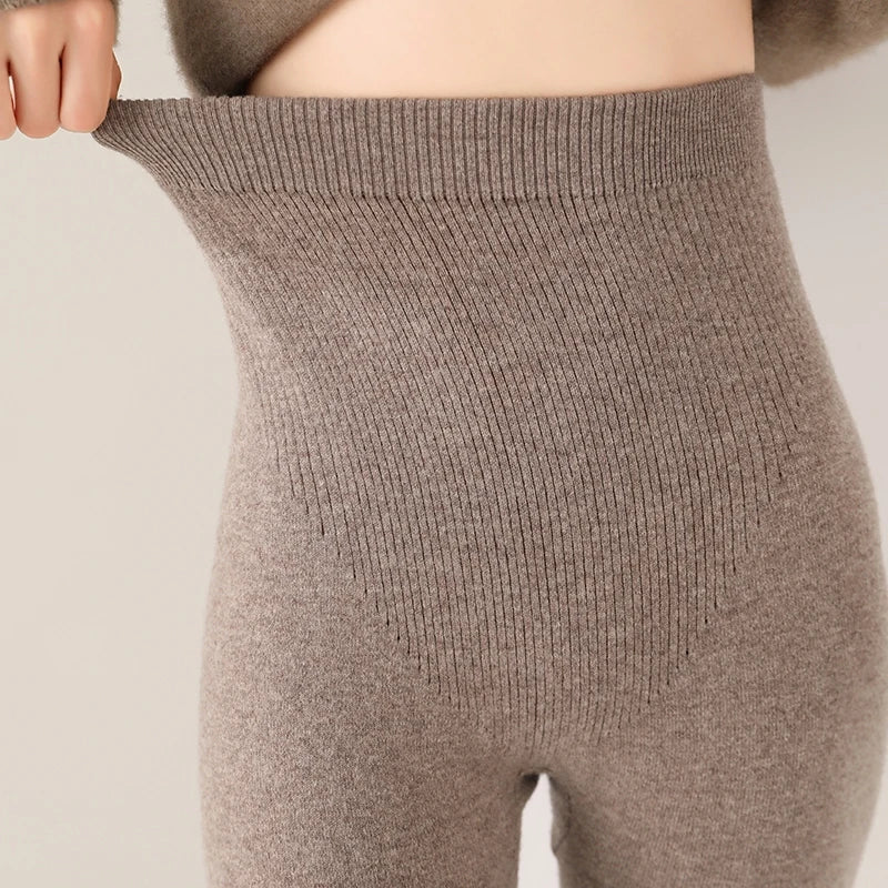 A person stretches the waistband of high-waisted leggings, revealing the elasticity and close fit of these ribbed, light brown knit pants. The image focuses on the waist and upper legs.