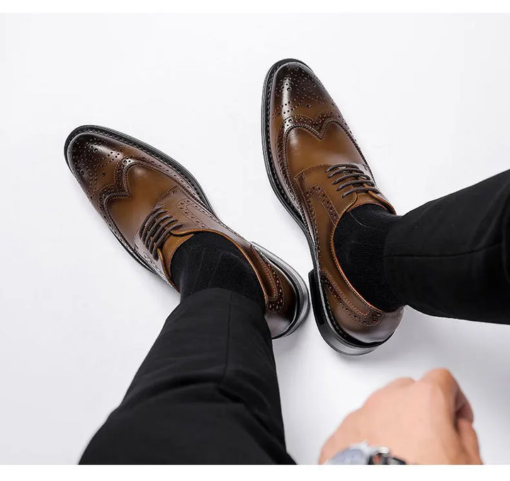 A person dressed in black pants and black socks is wearing brown premium leather brogue dress shoes with cushioned insole, sitting with legs slightly apart on a white background.
