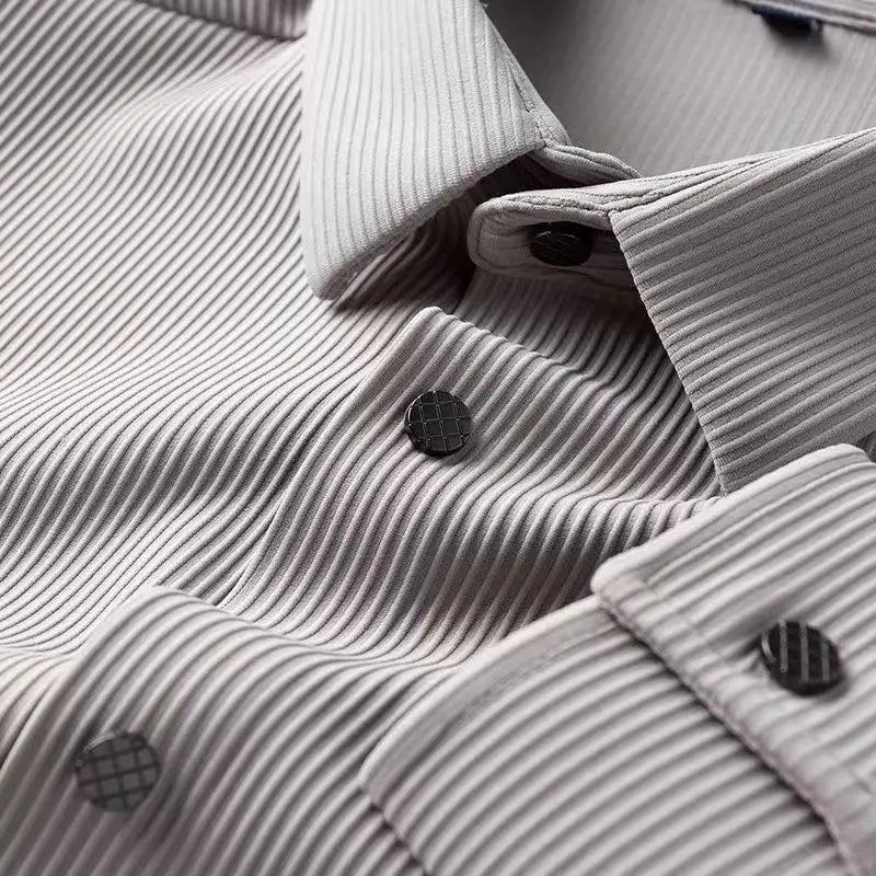 Close-up of a light gray, textured dress shirt with vertical ribbed patterns and dark buttons featuring a grid design. Crafted from wrinkle-resistant fabric, the shirt is neatly folded, highlighting the collar and front buttons.