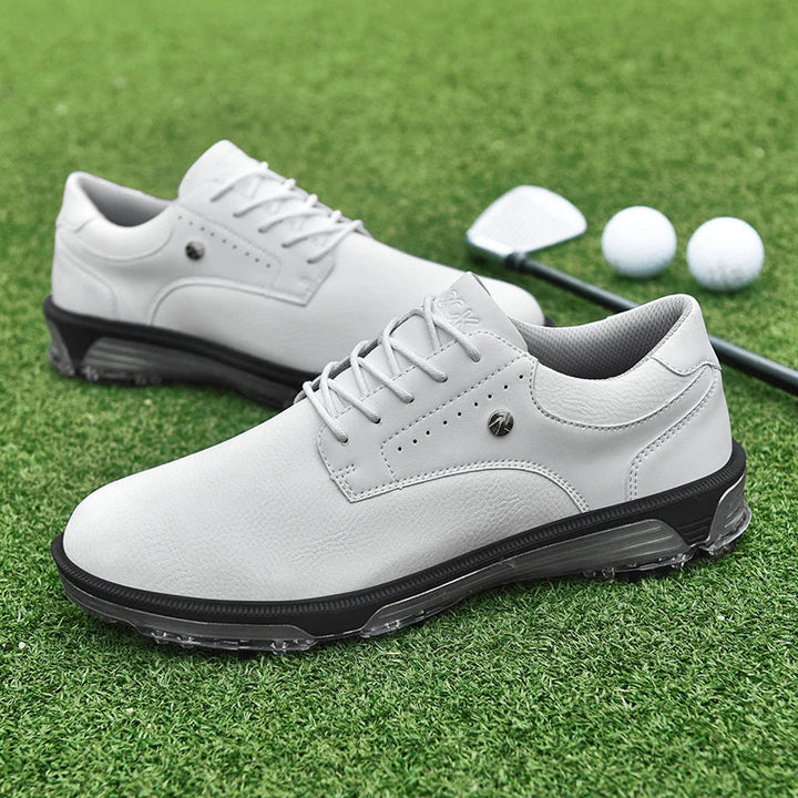 A pair of white golf shoes with black soles, featuring a reinforced toe cap, placed on green grass next to a golf club and two golf balls.