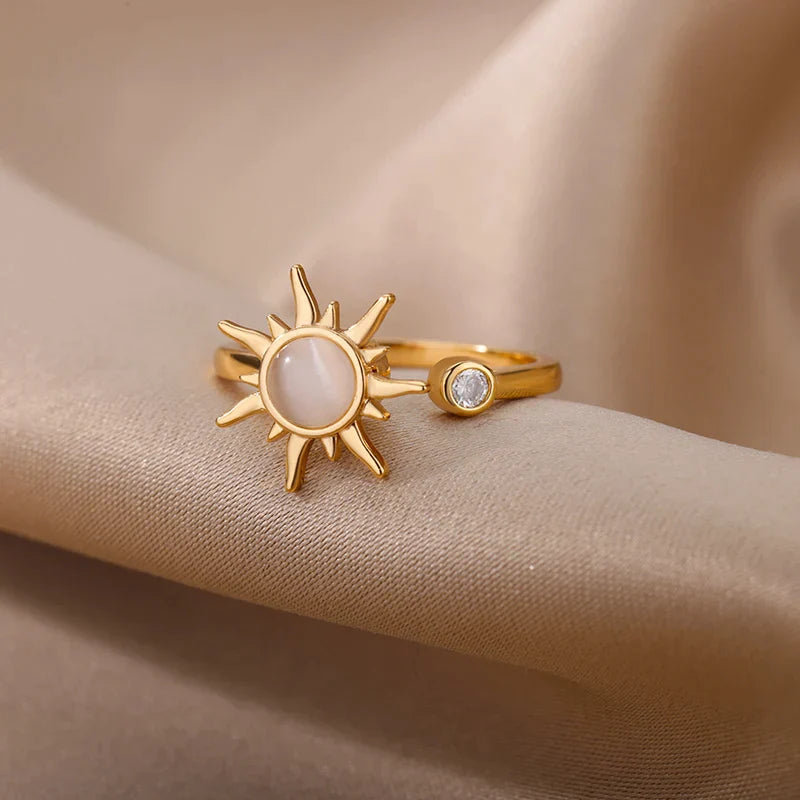 A sun ring crafted in gold features a radiant sun-shaped design with a round center gem and a smaller diamond set beside it, displayed on soft beige fabric. This adjustable gold ring adds celestial charm to any look.
