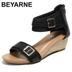 A single black wedge sandal with ankle and toe straps featuring gold buckles and subtle flash diamond embellishments, a tan footbed, and a woven-texture wedge heel. The brand name BEYARNE appears in black text at the top left.