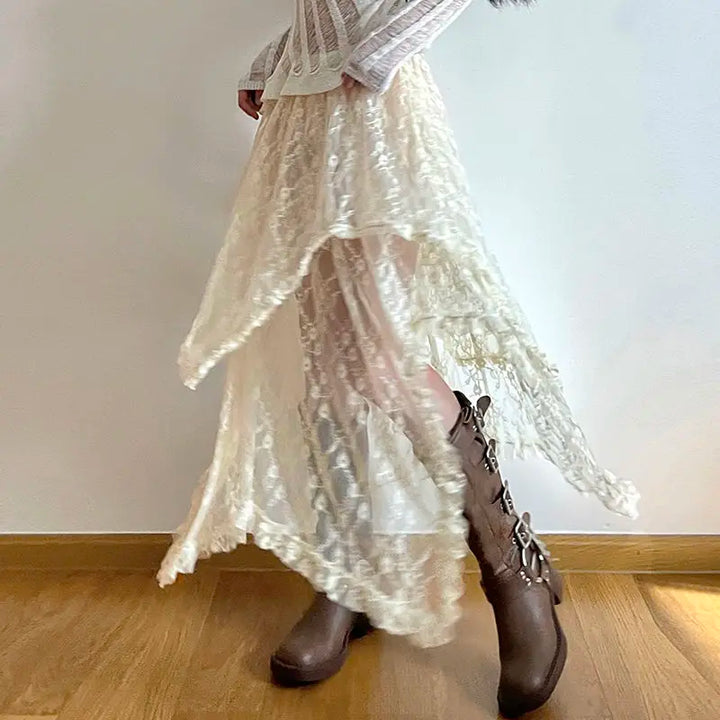 A person wearing a high-waist, asymmetrical cream silky lace skirt, a white long-sleeve top, and brown lace-up boots stands on a wooden floor against a plain white wall.