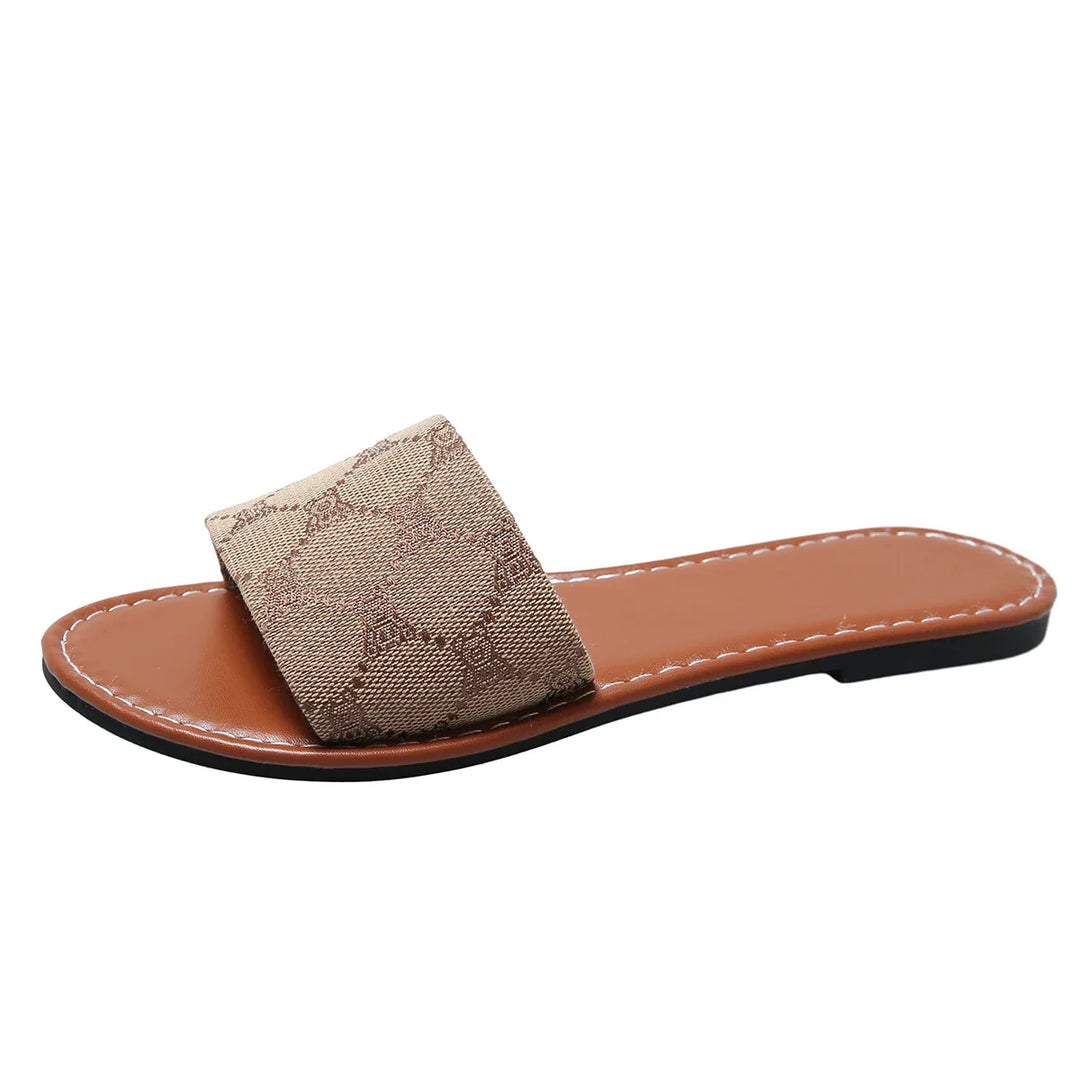A brown flat slide silhouette sandal by French Sole, featuring a wide beige fabric strap with a subtle geometric pattern and a stitched tan insole—perfect for lovers of timeless shoes.