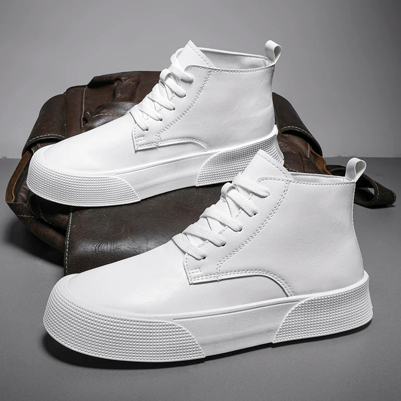 A pair of stylish, all-white vintage-inspired high-tops with textured soles and a cushioned footbed is displayed in front of a brown leather bag on a gray surface.