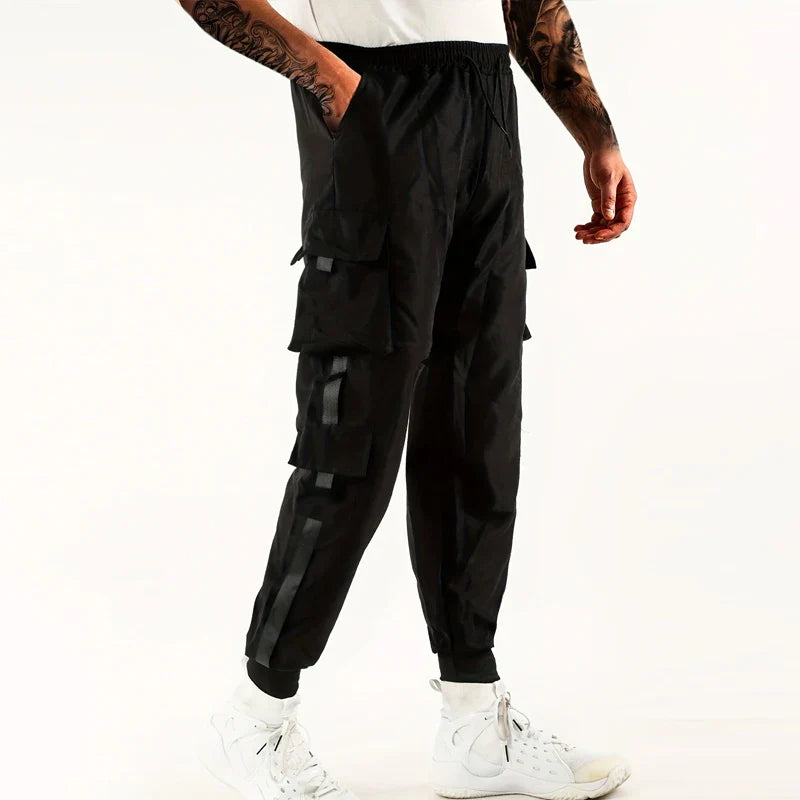A person wearing black cargo pants with ribbed ankle cuffs and an elastic waist, paired with a white shirt and white high-top sneakers, stands against a plain white background.
