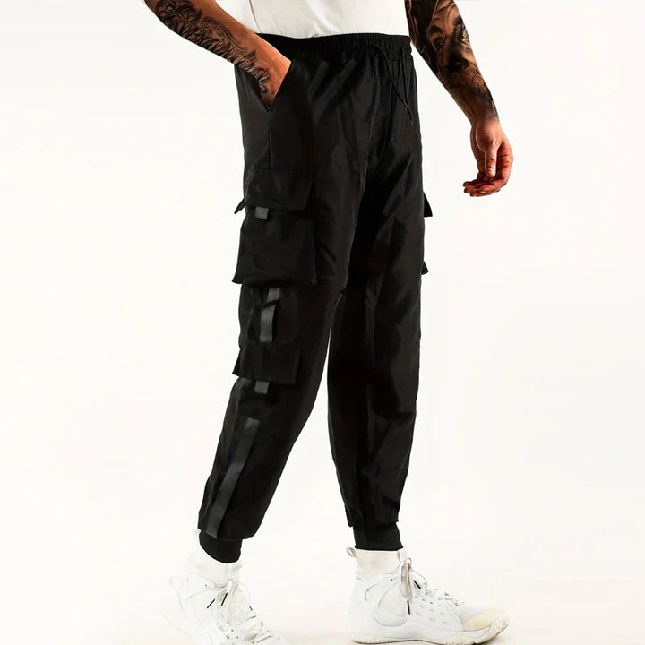 A person wearing black cargo pants with ribbed ankle cuffs and an elastic waist, paired with a white shirt and white high-top sneakers, stands against a plain white background.