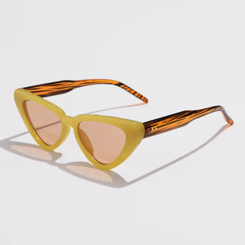 Cat-eye sunglasses with pale yellow frames, brown tinted lenses, and orange-and-black patterned arms offer UV400 sun protection. This lightweight eyewear is displayed on a white surface.