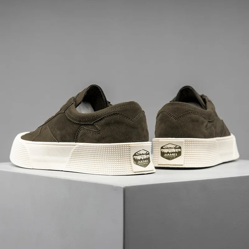 A pair of dark olive-green suede Lace-Up Sneakers with thick white textured soles are displayed on a gray platform. The back heel features a rectangular gold and black “JIAMEI” label with a mountain logo. Comfortable cushioning adds extra support.