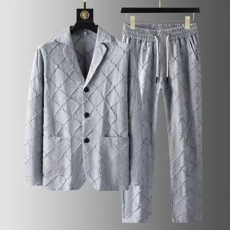 A light grey luxury two-piece set featuring a buttoned blazer with two pockets and matching relaxed fit trousers, both adorned with a quilted diamond pattern and hanging on black hangers against a grey gradient background.