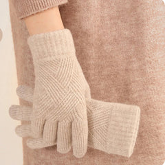 A person wearing a soft, beige cashmere blend sweater holds a pair of luxurious matching beige knit gloves with a subtle geometric pattern.