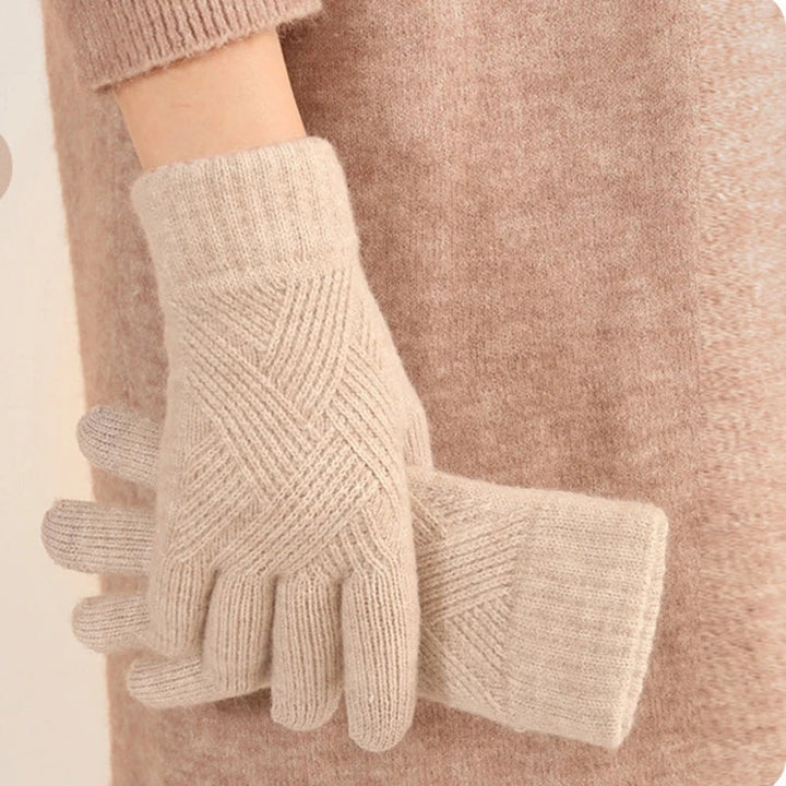 A person wearing a soft, beige cashmere blend sweater holds a pair of luxurious matching beige knit gloves with a subtle geometric pattern.