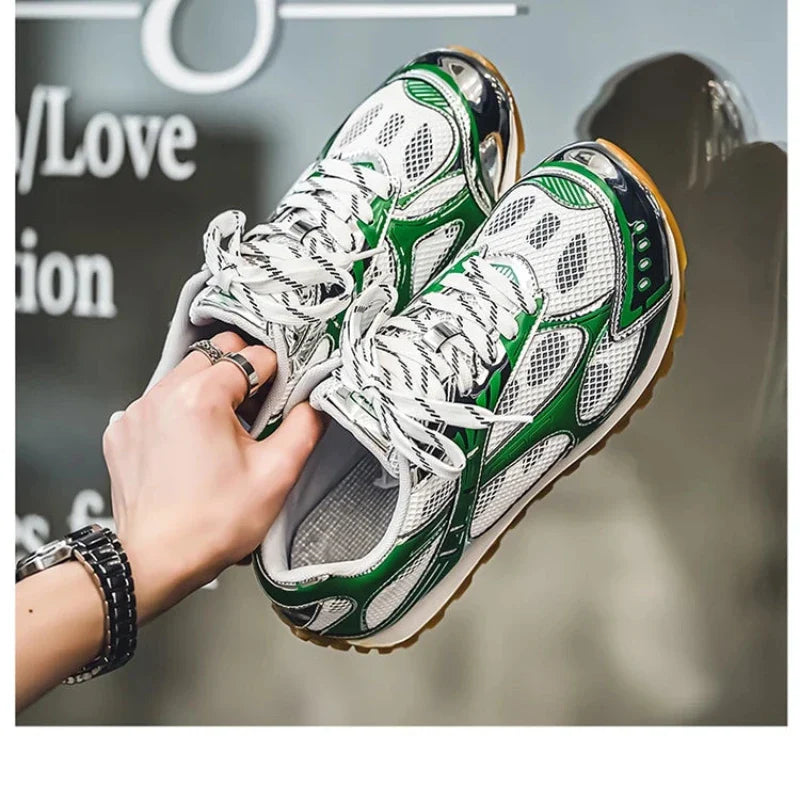 A hand holding a pair of stylish white lightweight mesh shoes with green and black accents, cushioned insoles, mesh panels, and striped laces, featuring a non-slip outsole against a blurred background with partial text.