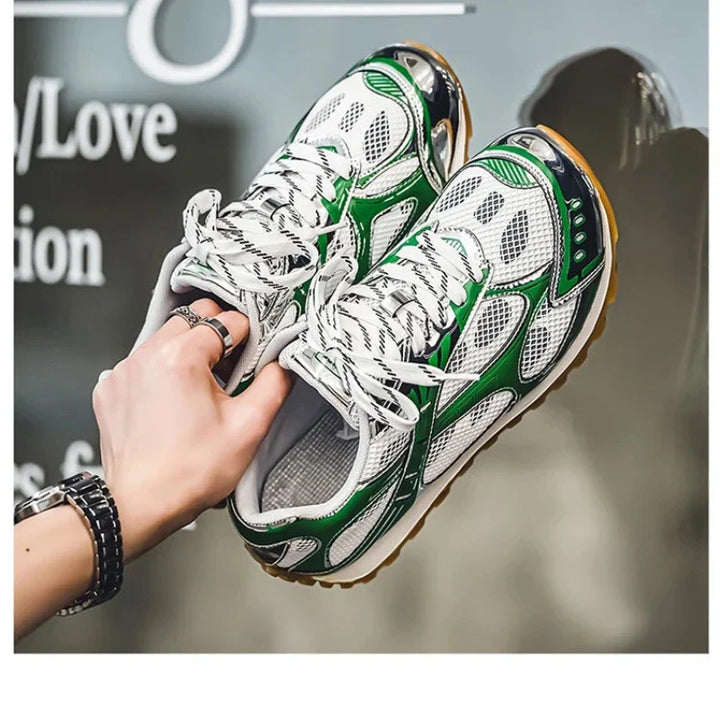 A hand holding a pair of stylish white lightweight mesh shoes with green and black accents, cushioned insoles, mesh panels, and striped laces, featuring a non-slip outsole against a blurred background with partial text.
