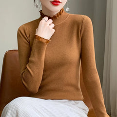 A woman wearing a fitted brown cashmere blend long-sleeve top with ruffled mock neck and cuffs, paired with a light-colored pleated skirt, sits on a brown chair. Her face is partially visible with red lipstick and dangling earrings.