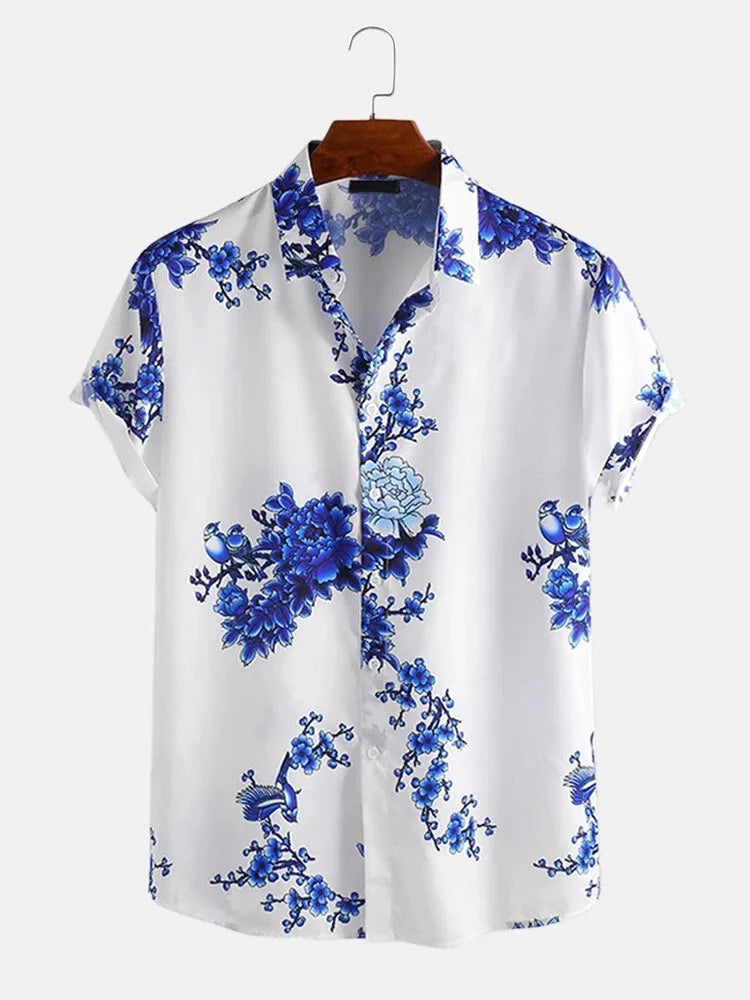 A summer-ready, short-sleeved white button-up shirt featuring a blue floral and branch pattern, crafted from a soft cotton-silk blend and displayed on a wooden hanger against a plain light background.
