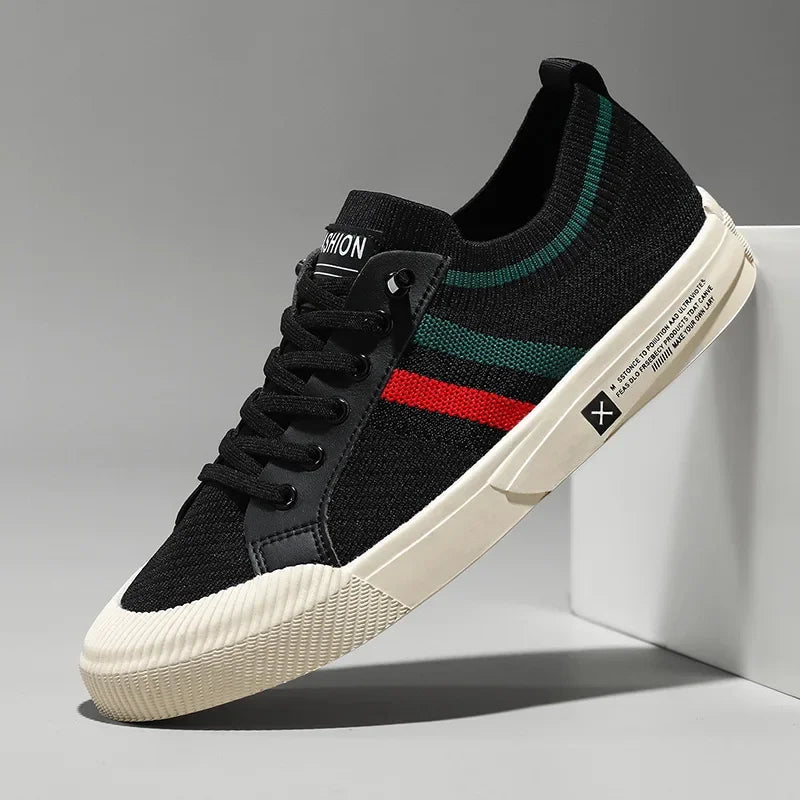 A black sneaker with a breathable mesh upper, white sole, green and red side stripes, black laces, and a knit texture rests against a white block on a gray background.