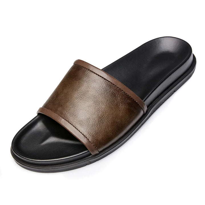 A single black slide sandal with a wide, dark brown genuine leather strap across the top and a slightly contoured footbed—an elevated take on men's luxury sandals.