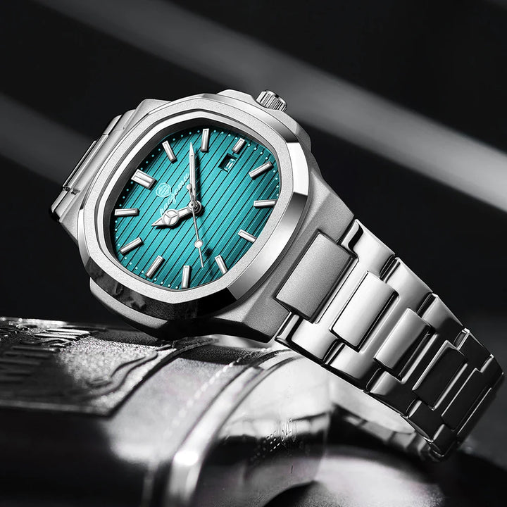 A luxury stainless steel wristwatch with a metallic band and a teal, striped dial featuring silver hour markers and hands, displayed on a reflective black and silver surface.