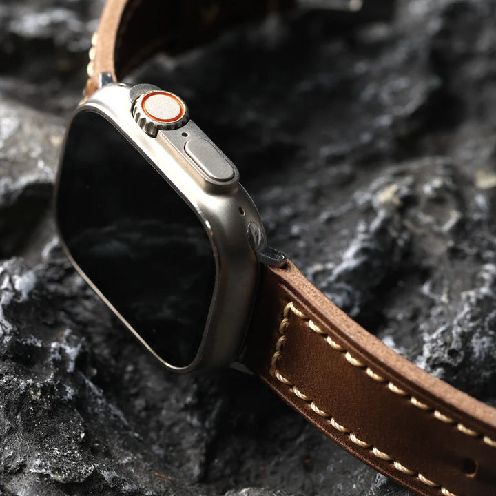 A close-up of a smartwatch with a handcrafted cowhide leather strap and silver casing, resting on a textured dark gray rock surface.