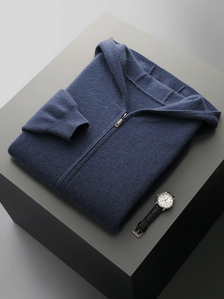 A neatly folded navy blue men's casual cardigan with a hood lies on a gray surface next to a black leather wristwatch with a white face.