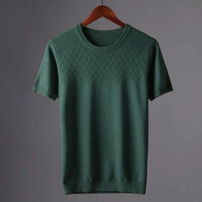 A green short-sleeve knit sweater in a classic fit hangs on a wooden hanger, featuring a diamond-pattern across the chest and a plain lower section, set against a neutral gray background.