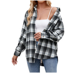A woman wears an oversized fit black and white plaid button-down shirt over a white tank top and blue jeans, with the shirt partially unbuttoned for effortless layering. Her hair is down against a plain white background.