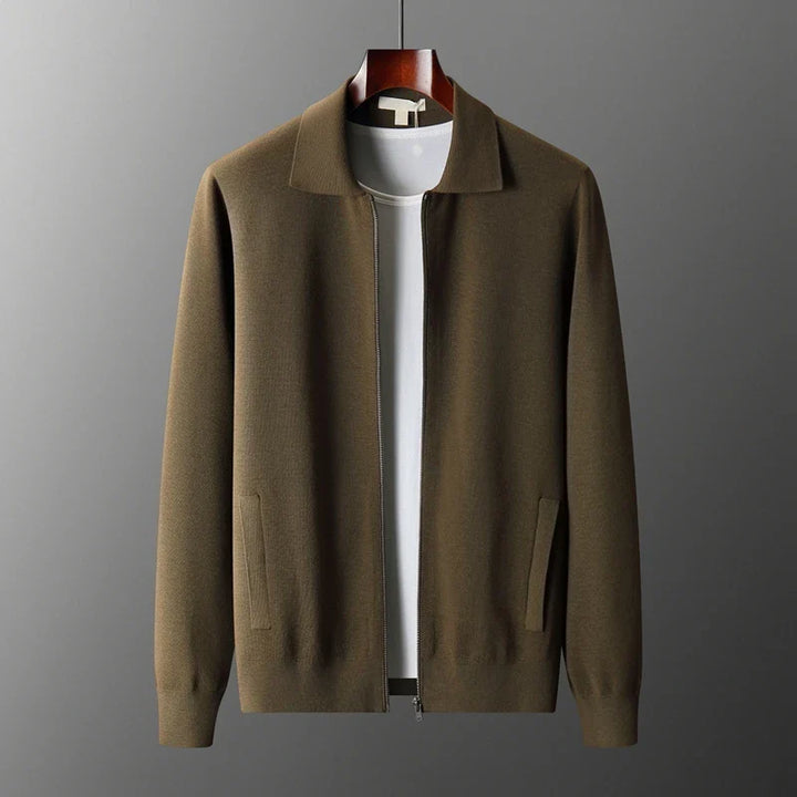 A brown zip-up merino wool jacket with a collar is displayed on a hanger over a plain white t-shirt, set against a plain gray background, offering natural temperature regulation.
