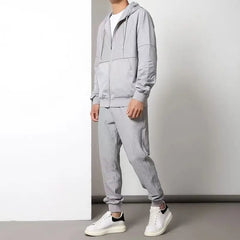 A person wearing a light gray activewear set, featuring a moisture wicking zipper hoodie and matching jogger pants with white sneakers, stands against a plain white and gray background. The persons face is not visible.
